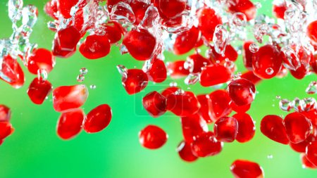 Photo for Fresh pomegranate pieces falling into water, green background - Royalty Free Image