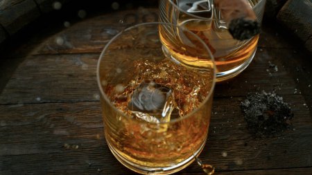Téléchargez les photos : Close-up of falling ice cube into glass of whiskey on old wooden barrel - en image libre de droit