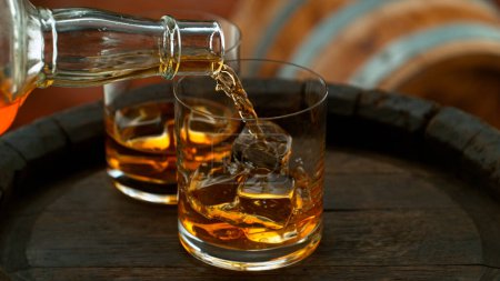 Téléchargez les photos : Close-up of pouring whiskey or rum on old wooden barrel - en image libre de droit