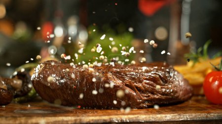 Téléchargez les photos : Gros plan sur la chute de sel sur un délicieux steak de boeuf dans la cuisine. - en image libre de droit