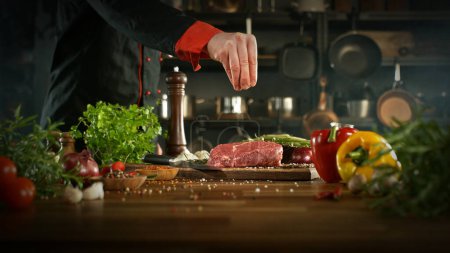 Téléchargez les photos : Gros plan sur la chute de sel sur un délicieux steak de bœuf dans la cuisine. Chef en arrière-plan. - en image libre de droit