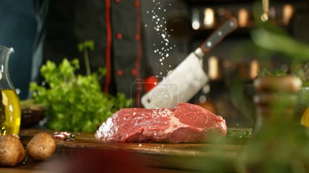 Téléchargez les photos : Gros plan sur la chute de sel sur un délicieux steak de bœuf dans la cuisine. Chef en arrière-plan. - en image libre de droit