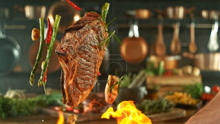 Foto de Primer plano de sabroso bistec de res volando por encima de la rejilla de hierro fundido con llamas de fuego - Imagen libre de derechos