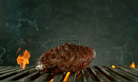 Photo for Close-up of tasty raw beef steak on cast-iron grate with fire flames - Royalty Free Image