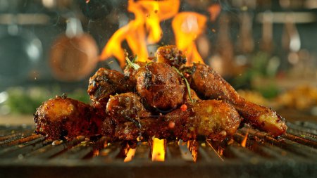 Foto de Primer plano de sabrosas patas de pollo en rejilla de hierro fundido con llamas de fuego - Imagen libre de derechos