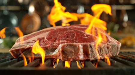 Foto de Primer plano de sabroso filete de carne cruda en rejilla de hierro fundido con llamas de fuego - Imagen libre de derechos