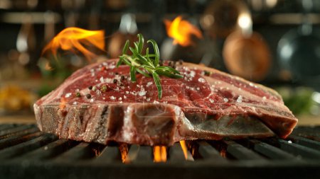 Foto de Primer plano de sabroso filete de carne cruda en rejilla de hierro fundido con llamas de fuego - Imagen libre de derechos