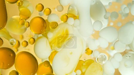 Freeze Motion Shot von sich bewegenden Öl- und Milchblasen auf goldenem Hintergrund, Kosmetikkonzept