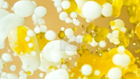 Freeze Motion Shot von sich bewegenden Öl- und Milchblasen auf goldenem Hintergrund, Kosmetikkonzept