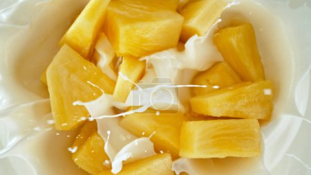 Photo for Fresh pineapple pieces falling into yoghurt cream, top down view - Royalty Free Image