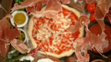 Foto de Super slow motion of falling pieces of ham on pizza dough with sugo, top down view - Imagen libre de derechos