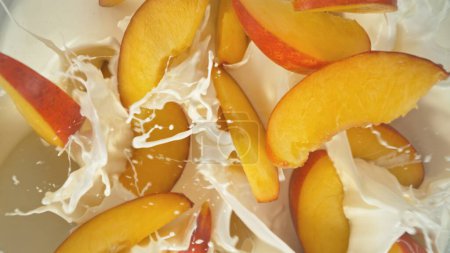 Fresh nectarines pieces falling into yoghurt cream, top down view