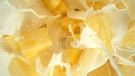 Photo for Fresh pineapple pieces falling into cream, top down view - Royalty Free Image