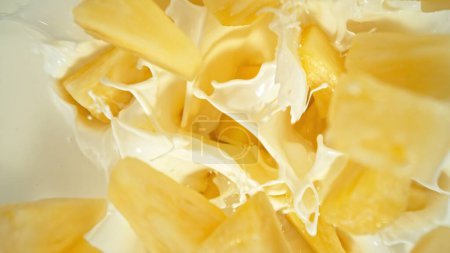 Téléchargez les photos : Pièces d'ananas frais tombant dans la crème, vue du haut vers le bas - en image libre de droit