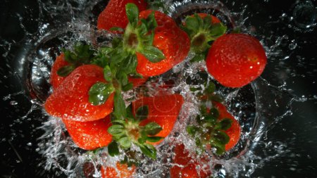 Photo for Fresh pieces of strawberries falling into water, top down view, black background - Royalty Free Image