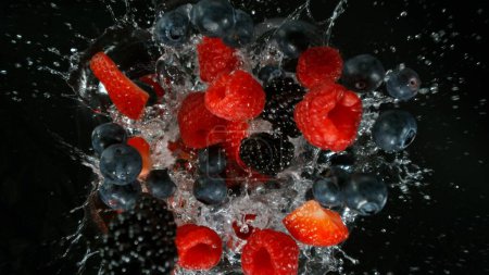 Fresh pieces of berries falling into water, top down view, black background
