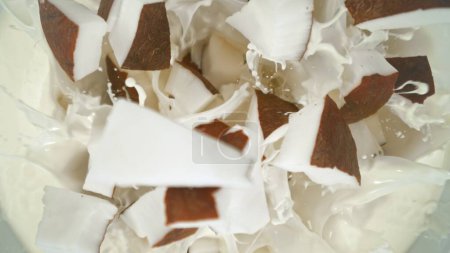 Piezas de coco fresco cayendo en crema, vista de arriba hacia abajo