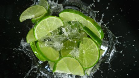 Photo for Fresh limes pieces falling into water, top down view - Royalty Free Image