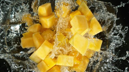 Fresh mango pieces falling into water, top down view
