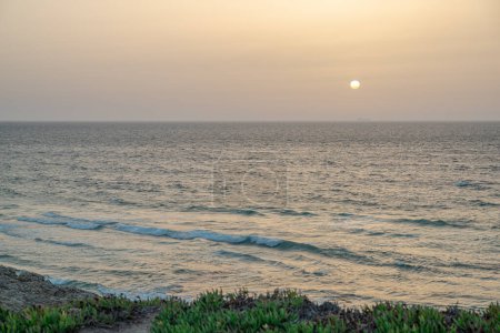 Téléchargez les photos : Beau coucher de soleil sur le rivage sablonneux de l'océan Atlantique calme. De longues vagues mousseuses approchent de la plage de sable. - en image libre de droit