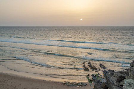 Foto de Hermosa puesta de sol en la orilla arenosa en el tranquilo océano Atlántico. Largas olas espumosas acercándose a la playa de arena. - Imagen libre de derechos