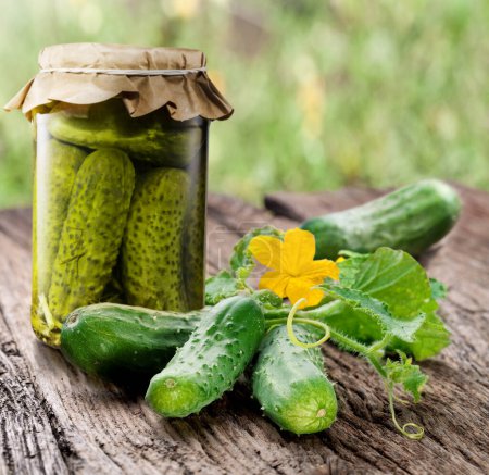 Photo for Fresh cucumbers and glass bottle with pickled cucumbers on old wooden table. - Royalty Free Image