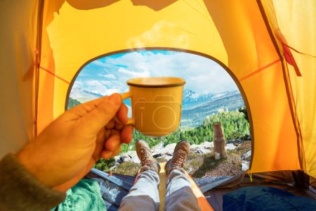 Photo for Cup of hot drink in the hand and wonderful view of mountain tops through the open entrance to the tent. The beauty of a romantic hike and camping accompanied by a dog. - Royalty Free Image