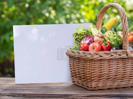 Photo for Variety of fresh organic vegetables and herbs in wicker basket. Blurred green nature at the background. Empty blank for your text, design or logo. - Royalty Free Image