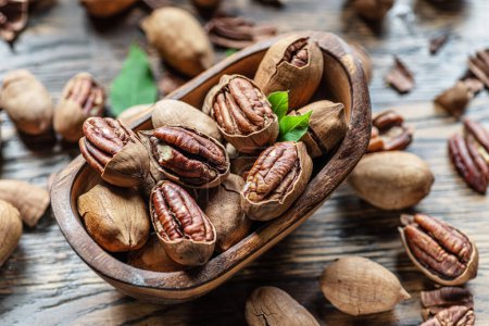 Photo for Shelled and cracked pecan nuts in the wooden bowl on wooden table. Top view. - Royalty Free Image