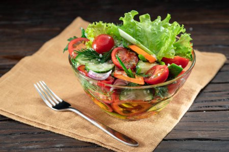 Téléchargez les photos : La salade de légumes avec des verts feuillus dans l'huile de verre est sur la table en bois. - en image libre de droit