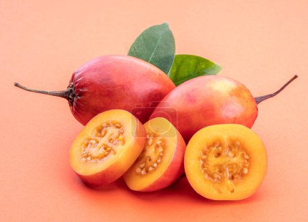 Reife Tamarillo-Früchte mit Scheiben und Tamarillo-Blättern auf orangefarbenem Hintergrund.