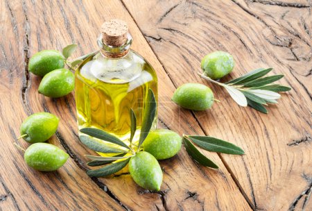 Foto de Aceitunas naturales verdes con botella de aceite de oliva sobre una antigua mesa de madera vintage. - Imagen libre de derechos