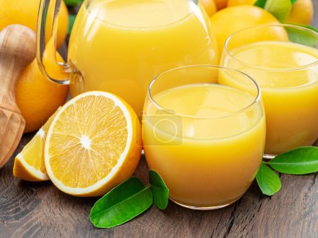 Photo for Glasses of fresh orange juice and orange fuits near them isolated on dark wooden background. Close up. - Royalty Free Image