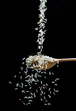 Foto de Granos de arroz blanco cayendo en la cuchara en el fondo negro. Comida popular e ingrediente principal de risotto y pilau. - Imagen libre de derechos