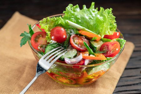 Téléchargez les photos : La salade de légumes avec des verts feuillus dans l'huile de verre est sur la table en bois. - en image libre de droit
