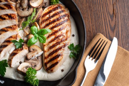 Photo for Roasted chicken fillet and mushrooms with herb in the frying pan on the wooden table close-up. - Royalty Free Image