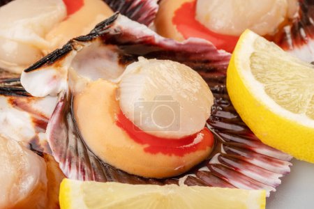 Foto de Group of fresh opened scallop with scallop roe or coral with lemon slices close up. - Imagen libre de derechos