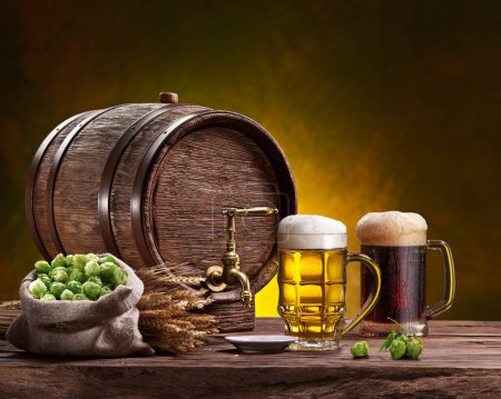 Foto de Two mugs of chilled beer, beer cask and bag of beer hops on wooden table. - Imagen libre de derechos