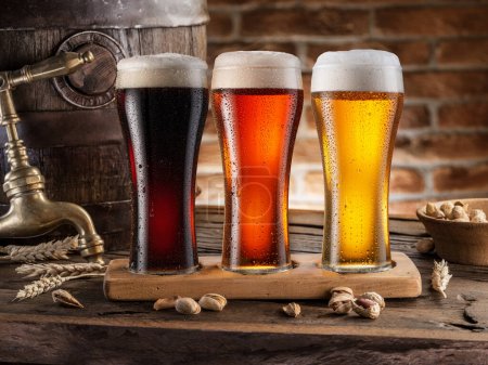 Téléchargez les photos : Trois verres réfrigérés de bière différente et baril de bière sur table en bois gros plan. - en image libre de droit