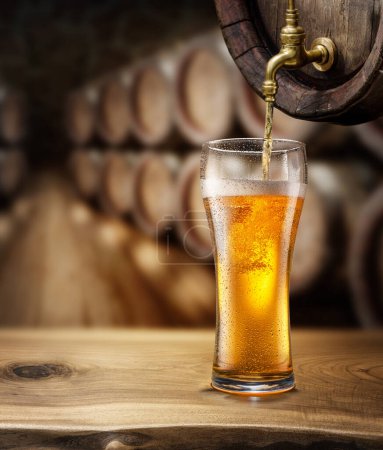 Photo for Pouring beer into a glass from wooden barrel. Blurred brewery cellar at the background. - Royalty Free Image