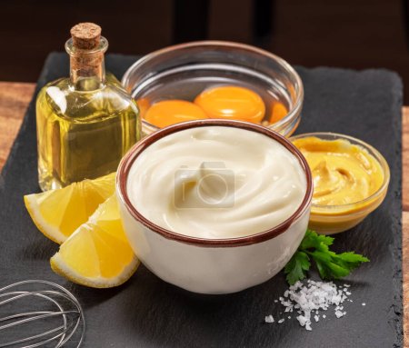 Téléchargez les photos : Mayonnaise maison et ingrédients de mayonnaise sur une assiette de service en ardoise noire. - en image libre de droit