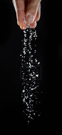 Photo for Male hand sprinkling edible salt at black background. - Royalty Free Image