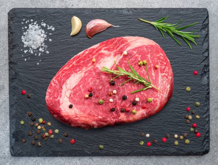 Foto de Raw ribeye steak on stone black serving plate. Flat lay. - Imagen libre de derechos