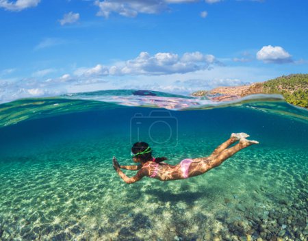 Photo for Girl diver is snorkeling on a beautiful sea beach. The lower half of the image is occupied by the seabed, the upper half by the coast and the sky. - Royalty Free Image