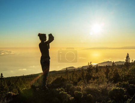 Téléchargez les photos : Silhouette de femme avec caméra. Femme prend une photo de l'île de La Gomera dans les rayons du soleil couchant. Île de Tenerife. - en image libre de droit