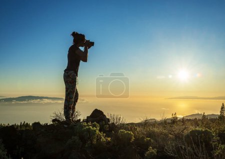 Foto de Silueta de mujer con cámara. Mujer toma una foto de la isla de La Gomera en los rayos del sol poniente. Isla de Tenerife. - Imagen libre de derechos
