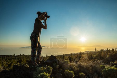 Téléchargez les photos : Silhouette de femme avec caméra. Femme prend une photo de l'île de La Gomera dans les rayons du soleil couchant. Île de Tenerife. - en image libre de droit