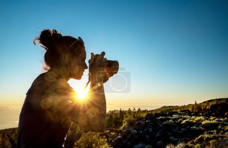 Téléchargez les photos : Silhouette of woman with camera. Woman takes photo of La Gomera Island in the rays of the setting sun. Tenerife Island. - en image libre de droit