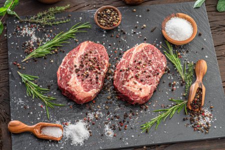 Photo for Raw Ribeye steaks with salt and herbs on grey board. Top view. - Royalty Free Image