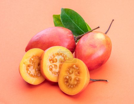 Photo for Ripe tamarillo fruits with slices and tamarillo leaves isolated on a orange background. - Royalty Free Image